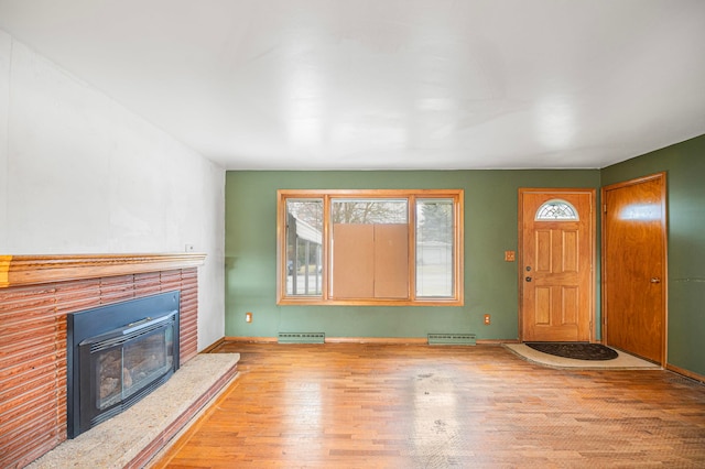 unfurnished living room with light hardwood / wood-style floors, a brick fireplace, and a baseboard radiator