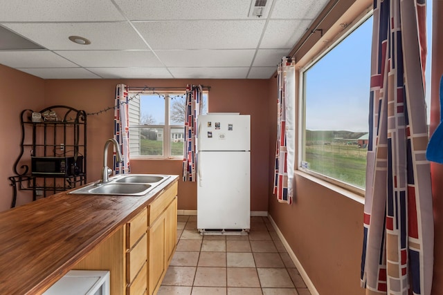 kitchen with a paneled ceiling, light brown cabinets, sink, light tile patterned floors, and white fridge