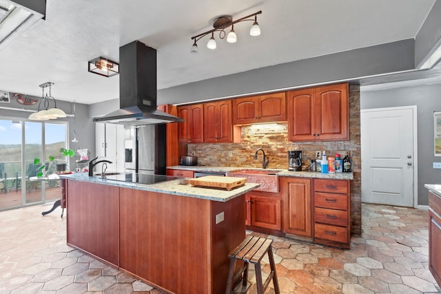 kitchen featuring tasteful backsplash, island exhaust hood, a center island with sink, and pendant lighting