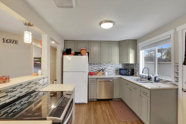 kitchen with sink, decorative light fixtures, decorative backsplash, appliances with stainless steel finishes, and light wood-type flooring