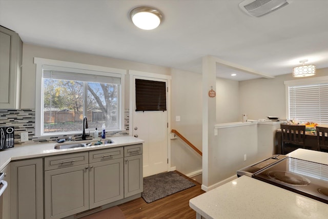 kitchen featuring gray cabinetry, stove, backsplash, sink, and wood-type flooring