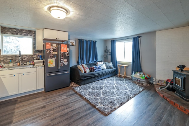 living room with plenty of natural light, sink, a wood stove, and dark wood-type flooring