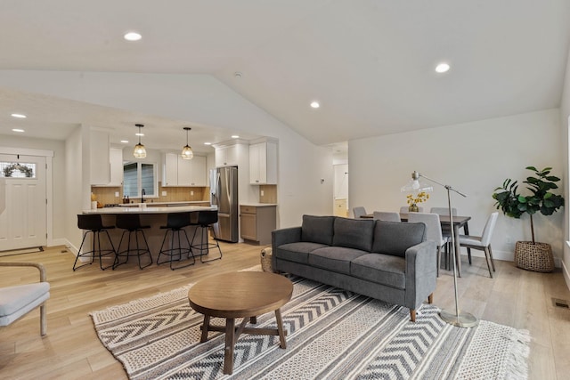 living room featuring sink, vaulted ceiling, and light wood-type flooring