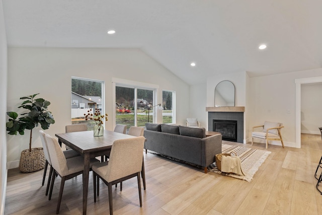 dining room featuring light hardwood / wood-style floors, vaulted ceiling, and a tiled fireplace