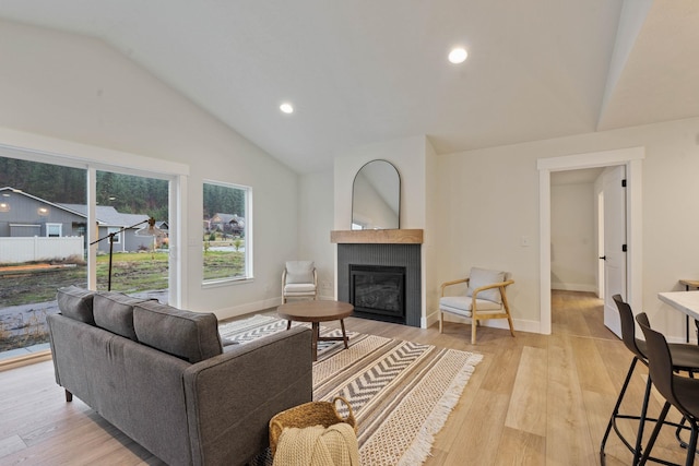 living room featuring light hardwood / wood-style flooring, lofted ceiling, and a tiled fireplace