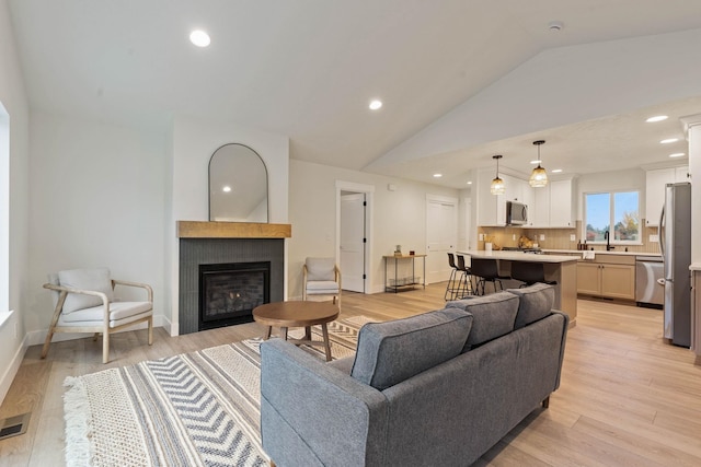 living room with a fireplace, light hardwood / wood-style floors, lofted ceiling, and sink