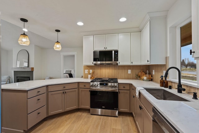 kitchen featuring kitchen peninsula, appliances with stainless steel finishes, light hardwood / wood-style flooring, white cabinetry, and hanging light fixtures