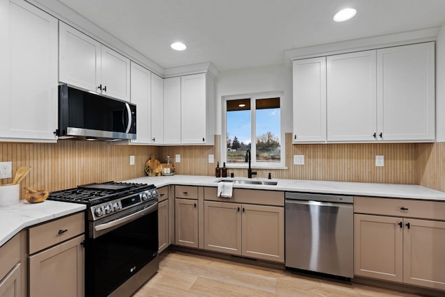 kitchen featuring sink, stainless steel appliances, light stone counters, white cabinets, and light wood-type flooring