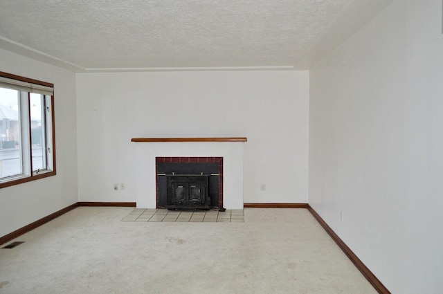 unfurnished living room with a tiled fireplace, a textured ceiling, and light carpet