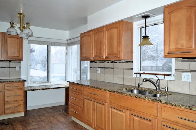 kitchen with dark stone counters, backsplash, hanging light fixtures, and sink