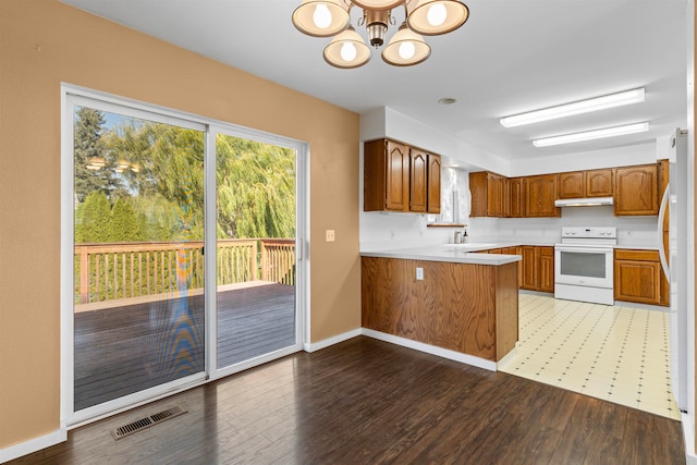 kitchen with kitchen peninsula, dark hardwood / wood-style flooring, white appliances, sink, and an inviting chandelier