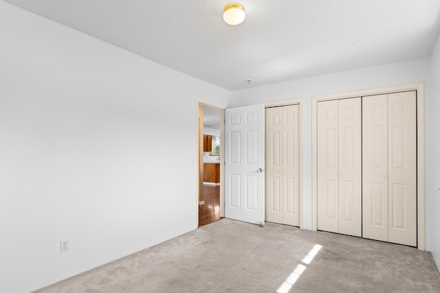 unfurnished bedroom featuring light carpet and two closets