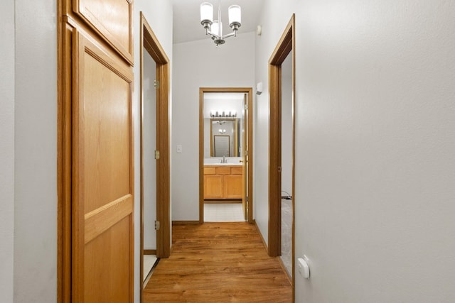 corridor with lofted ceiling, light wood-type flooring, and an inviting chandelier