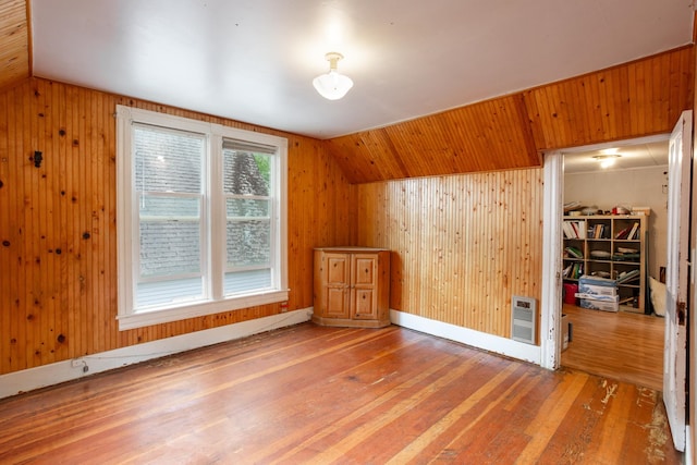 additional living space with heating unit, wood walls, vaulted ceiling, and hardwood / wood-style flooring