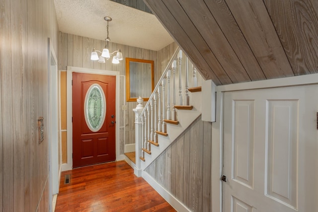 foyer with a textured ceiling, vaulted ceiling, wooden walls, a chandelier, and hardwood / wood-style floors