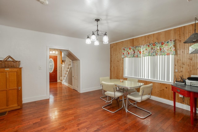 dining area with wooden walls, a chandelier, and dark hardwood / wood-style floors