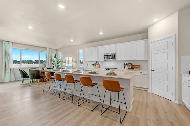 kitchen with white cabinetry, a kitchen island with sink, and light hardwood / wood-style flooring