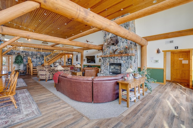 living room featuring high vaulted ceiling, a stone fireplace, beam ceiling, light hardwood / wood-style floors, and wood ceiling