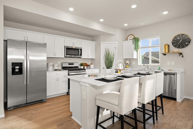 kitchen featuring white cabinets, light wood-type flooring, a kitchen island, a kitchen bar, and stainless steel appliances