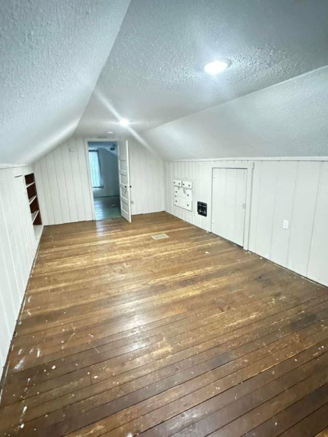 bonus room with a textured ceiling, lofted ceiling, wooden walls, and dark wood-type flooring