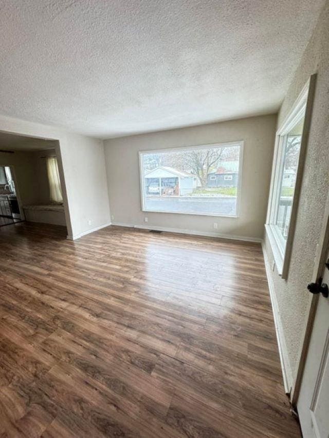 unfurnished living room with a textured ceiling and dark wood-type flooring