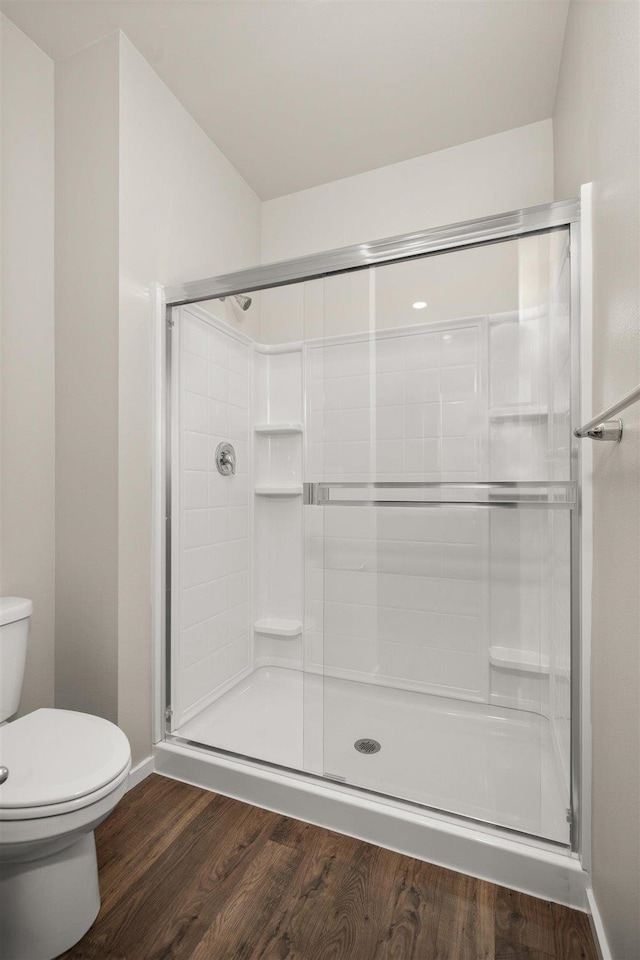 bathroom with hardwood / wood-style floors, a shower with shower door, and toilet