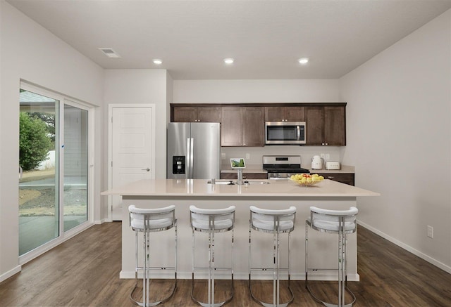 kitchen with dark hardwood / wood-style flooring, a kitchen island with sink, appliances with stainless steel finishes, and a breakfast bar area