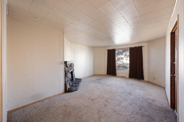 empty room featuring wooden walls, visible vents, light colored carpet, and a stone fireplace