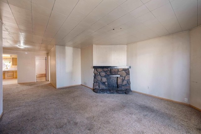 unfurnished living room featuring a stone fireplace, carpet flooring, and baseboards