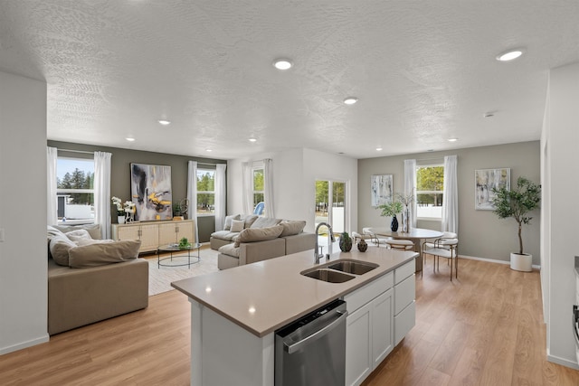 kitchen with light wood-type flooring, dishwasher, a center island with sink, and a sink