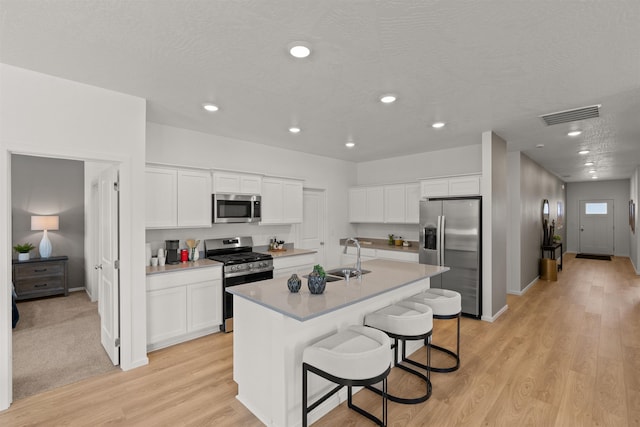 kitchen with a sink, visible vents, white cabinetry, appliances with stainless steel finishes, and a center island with sink