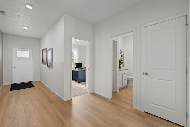 entryway with baseboards, a textured ceiling, visible vents, and light wood-style floors