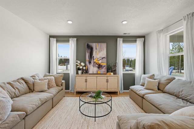 living area with a wealth of natural light, visible vents, a textured ceiling, and wood finished floors