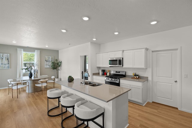 kitchen with white cabinets, a breakfast bar area, stainless steel appliances, light wood-type flooring, and a sink