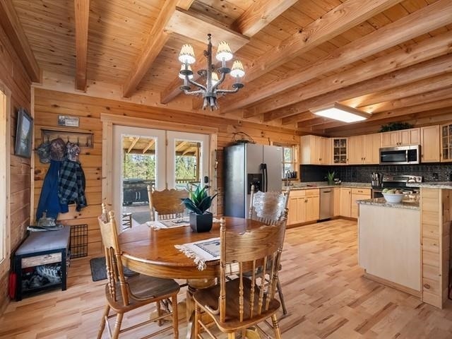 dining room featuring a chandelier, wood walls, beamed ceiling, and light hardwood / wood-style floors