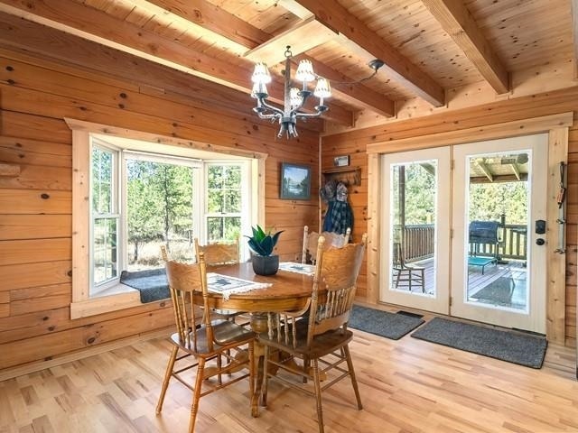 dining space featuring light wood-type flooring, wood ceiling, wooden walls, beam ceiling, and an inviting chandelier