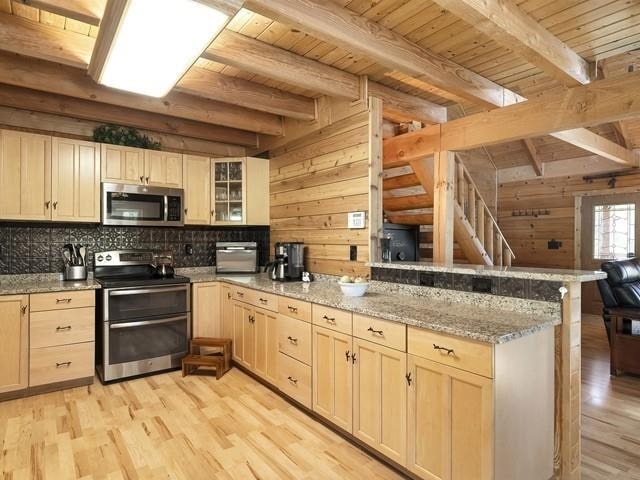 kitchen featuring kitchen peninsula, beam ceiling, stainless steel appliances, and wood walls