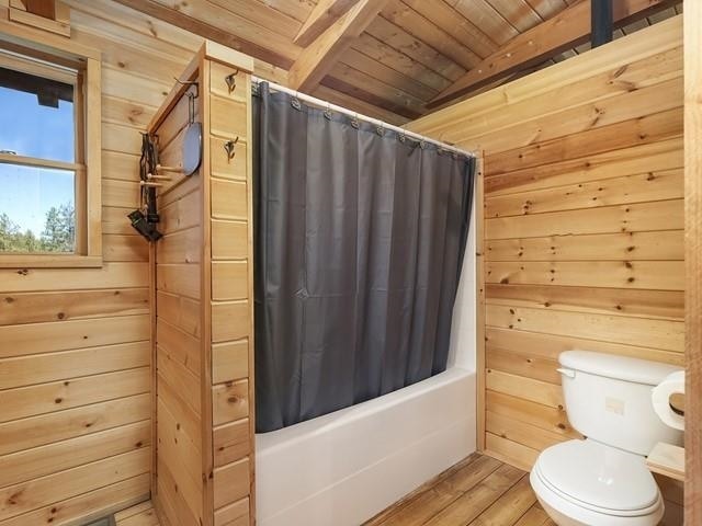 bathroom with hardwood / wood-style flooring, wooden ceiling, beamed ceiling, toilet, and wood walls