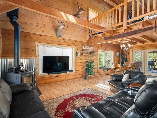 living room featuring wood-type flooring, a notable chandelier, beamed ceiling, a wood stove, and wood walls