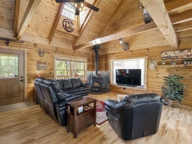 living room with light wood-type flooring, beam ceiling, high vaulted ceiling, a wood stove, and wood walls