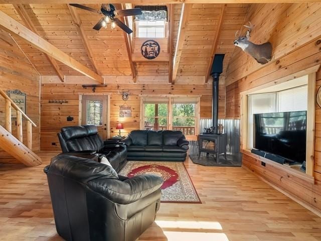 living room featuring a wood stove, wooden ceiling, vaulted ceiling with beams, wood walls, and light hardwood / wood-style floors