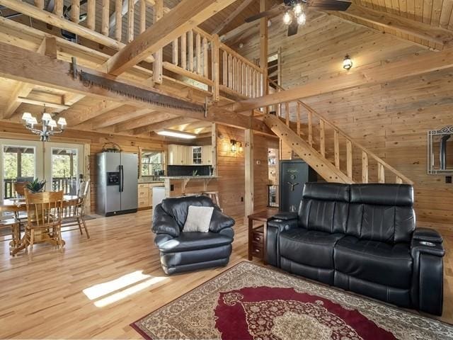 living room with high vaulted ceiling, ceiling fan with notable chandelier, wooden walls, beamed ceiling, and wood-type flooring