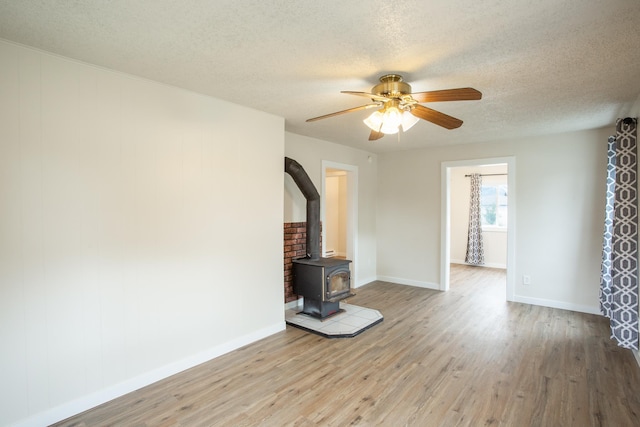 unfurnished living room featuring ceiling fan, light wood-type flooring, a wood stove, and a textured ceiling