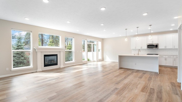 kitchen featuring a tile fireplace, white cabinets, hanging light fixtures, light wood-type flooring, and an island with sink