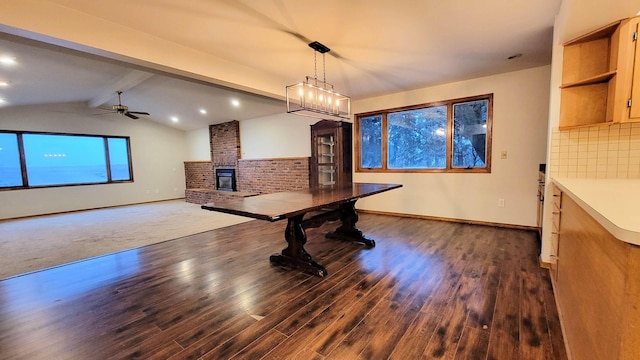 dining space with a brick fireplace, vaulted ceiling with beams, baseboards, a ceiling fan, and dark wood-style flooring