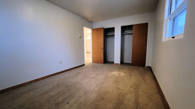 unfurnished bedroom featuring light colored carpet, baseboards, and two closets