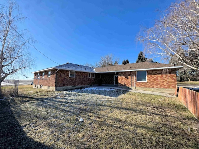 back of house featuring fence, brick siding, and a lawn