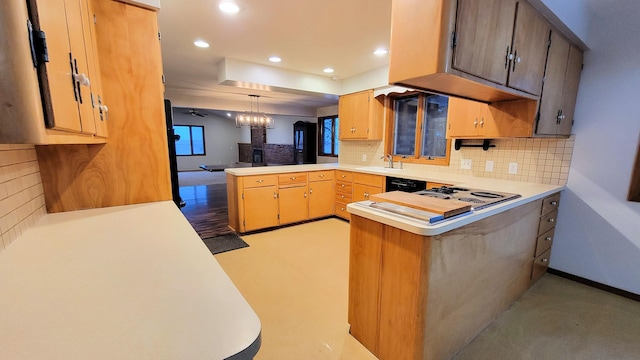 kitchen with a peninsula, stovetop, a sink, decorative backsplash, and light countertops