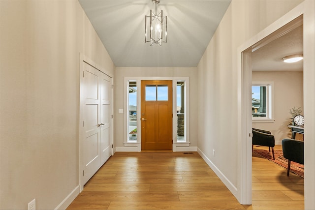 foyer featuring an inviting chandelier, lofted ceiling, and light wood-type flooring