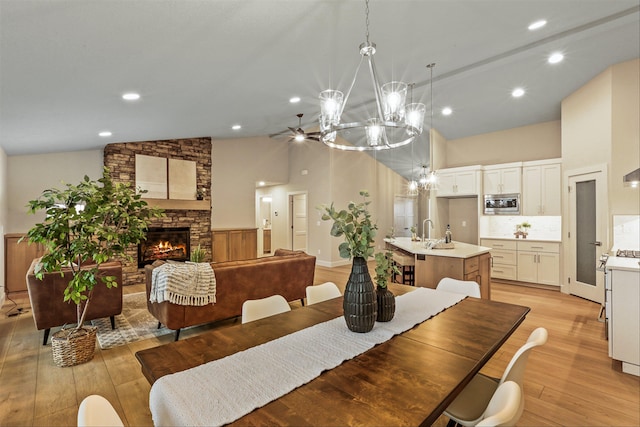 dining area with high vaulted ceiling, sink, light hardwood / wood-style flooring, a fireplace, and a notable chandelier